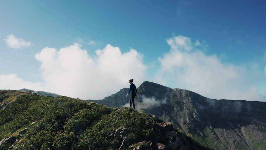 Young brave brunette girl climbing the mount, enjoying panorama, feeling freedom; thick clouds moving around; natural beauty of Caucasus mountain ridges; active sport lifestyle; aerial drone view Royalty-Free Stock Footage #1038592430