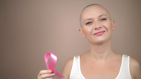 beautiful bald woman holds a pink ribbon in her hands. gentle pastel background.