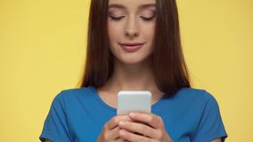 selective focus of girl texting on smartphone isolated on yellow