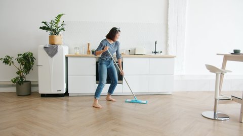 Happy young woman cute housewife is washing floor with mop and dancing at home in kitchen enjoying housework. People, modern lifestyle and youth concept.