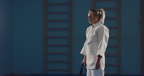 Beautiful girl fighter ties a black belt on a kimono, preparing for battle. Athlete is waiting for the fight.