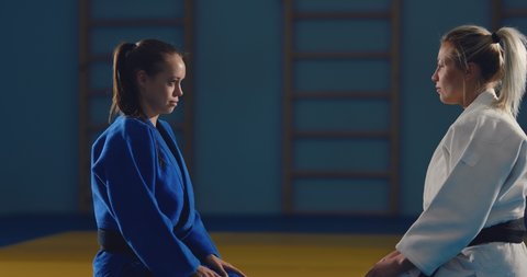 Beautiful judoka girls are sitting on the tatami, preparing for training. Careful look, the opponents are looking at each other.