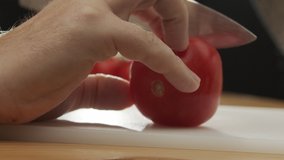Close-up man's hands cut fresh tomato with sharp knife. Slow motion video