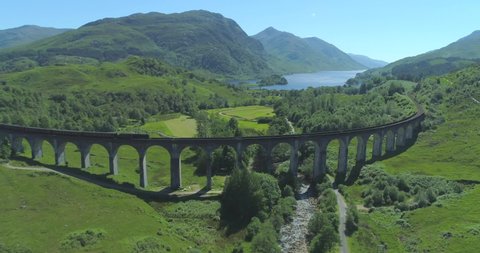 Wide aerial of Hogwart's Express (Harry Potter) steam train travelling over the Glen Finnan Viaduct in the Scottish Highlands with Loch Shiel in the background on a sunny day