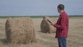 smart farming agriculture concept. lifestyle man worker farmer studying a haystack in a field on digital tablet. slow motion video. male agronomist botanist farmer working in the field