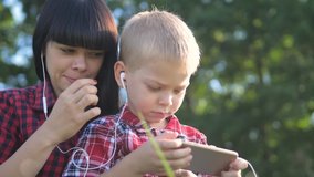 happy family funny video slow motion play music teamwork outdoors. Mom and son listen to music on lifestyle smartphone in same headphones for two. happy family mother woman and son little boy spend