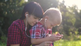 happy family funny video play music slow motion teamwork outdoors. Mom lifestyle and son listen to music on smartphone in the same headphones for two. happy family mother woman and son little boy