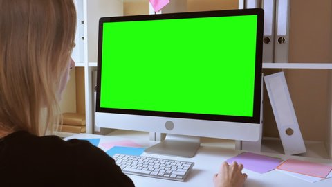 side view woman with blond hair sitting in front of computer with green screen. unrecognizable businesswoman moving pc mouse looking on display. employee sitting at white desk in office