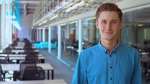 portrait young caucasian business man posing in modern office. millennials at workplace wearing denim shirt looking at the camera