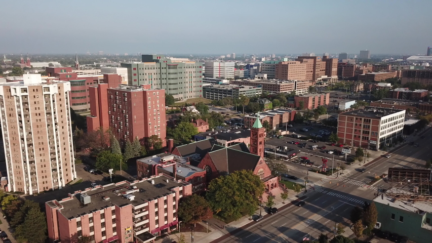 Aerial Drone Footage of Woodward Ave. Detroit museums, church, skyline and traffic visible on a beautiful sunny day. Public transportation, and people walking by on the city streets.