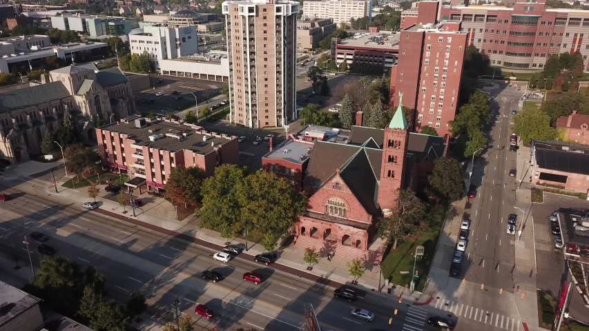 Aerial Drone Footage of Woodward Ave. Detroit museums, church, skyline and traffic visible on a beautiful sunny day. Public transportation, and people walking by on the city streets.