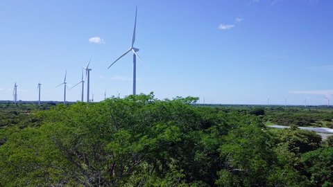 aerial view of wind turbine, trees, on sunny day, droneing up and pan