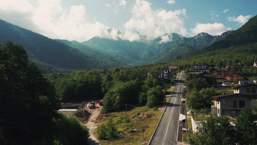 Aerial scenic view; drone flying forward over street of village Krasnaya Polyana; caucasus mountains on background; quiet life in mountain hamlet; rural terrain, beautiful light summer cloudy day Royalty-Free Stock Footage #1038622313