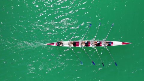 Aerial drone top down view video of sport canoe operated by team of young women in emerald sea