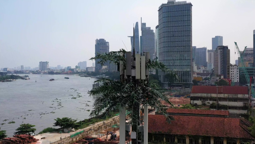 slow panning R to L aerial shot of ultra modern mobile phone tower disguised as a palm tree against a background of a riverfront construction site with city buildings, cranes and boat traffic - Powered by Shutterstock - Get 15% off with code: PIKWIZARD15