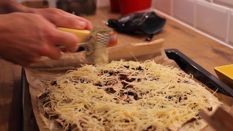 close up of hands grating cheese on top of pizza or flammekueche with mushrooms, cooking at home kitchen