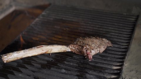 Single tomahawk rib steak on hot black grill with flames underneath.
