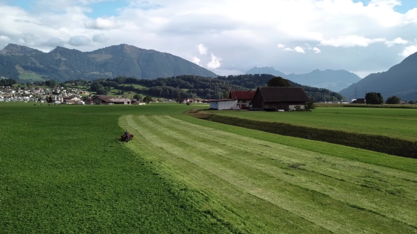 Farmer mows field in front of village nestled in the middle of the mountains