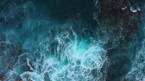 Top down abstract aerial view of ocean waves crashing on rocky shoreline