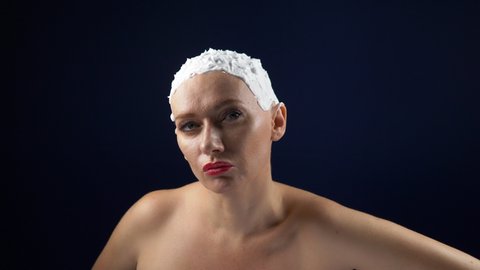 a woman in a leather corset shaves her head covered in shaving foam with a dangerous razor. dark background