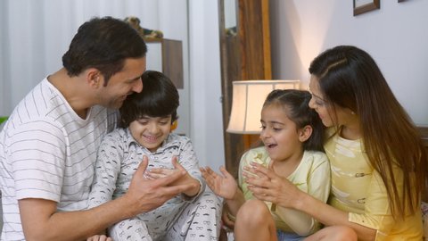 Smiling Indian parents playing with their cute children before going to sleep - playtime in bed. Happy carefree family from India - Young couple sitting together in bed with their son and daughter,...