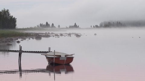 Morning mist view of a calm lake with a rowboat tied to a small jetty. Summer in northern Sweden when it never gets dark (Norrbotten County).
