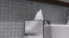 4K video of tissue box with white tissue protruding, Caucasian young to middle age woman’s hand appears, takes and pulls three tissues out of the box. A person grabbing tissues. Full hd video.
