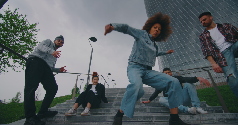 A group of young urban dancers of are having fun to move with colorful neon glowing strings splashing effect in a city center with skyscrapers.