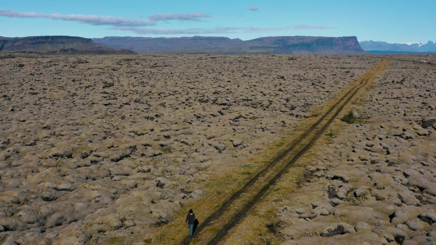 Aerial view of a woman walking next to green Lava fields moss-covered hills. Southern Iceland.