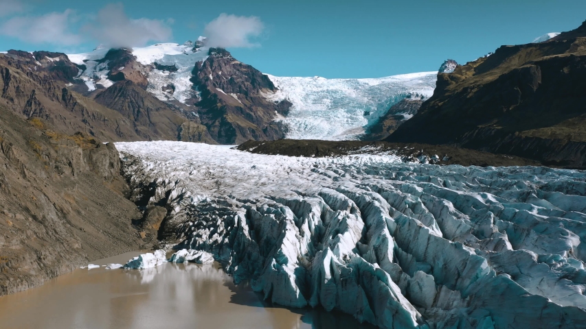 Flying above patterns and details of white glacier with black volcanic ash on a frozen iceberg on a sunny day in Vatnajokull National Park, southern Iceland