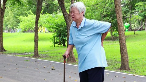 Asian senior woman with hip joint pain while walking,female patient having backache,lumbago pain,hands touching on the hip in outdoor park,elderly people suffering from ribbing pain or waist pain,4K