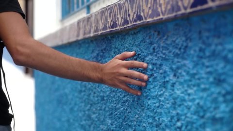 man walks and grazes hand on blue wall in Chefchaouen, Morocco.