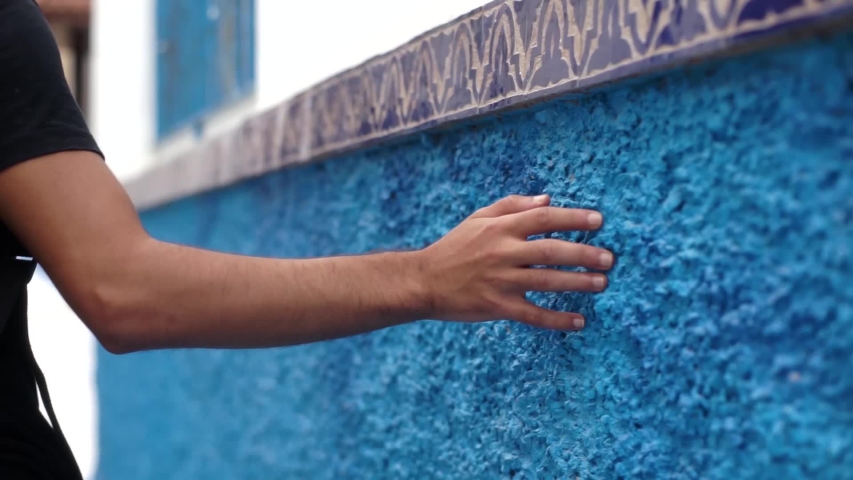 man walks and grazes hand on blue wall in Chefchaouen, Morocco.