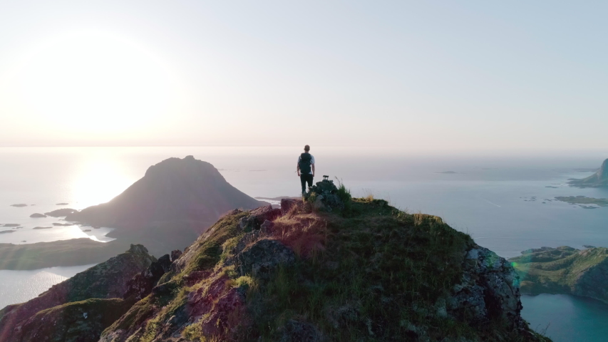 4K drone shot of Norwegian climber celebrating reaching the top of a mountain by raising his arms to the sky with a panorama sunset background view of Lofoten and Vesterålen in Norway. Royalty-Free Stock Footage #1038703259