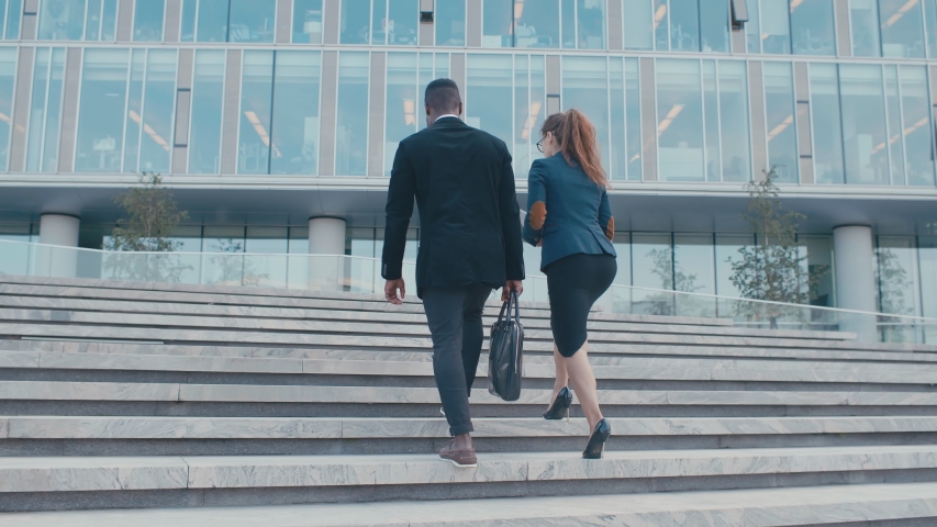 Young business people colleagues returning from their break. Man and woman in formal suits going up stairs into office building. Multi racial partnership, communication business people concept