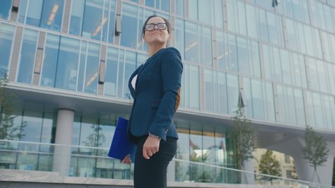 First day at new job concept, young happy confident businesswoman standing in front of modern glass office center near entrance, just hired smiling ready to start work in big company, motivational