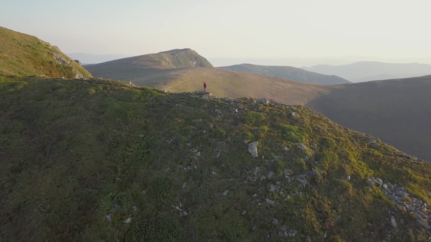 Hiker standing on top of rocky mountain enjoying magnificent view. Mountaineer looking at sunrise in mountains.