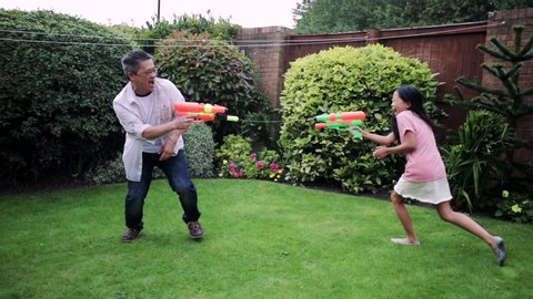 Family are having a water fight in the garden with water pistols. They children are being chased by their father.
