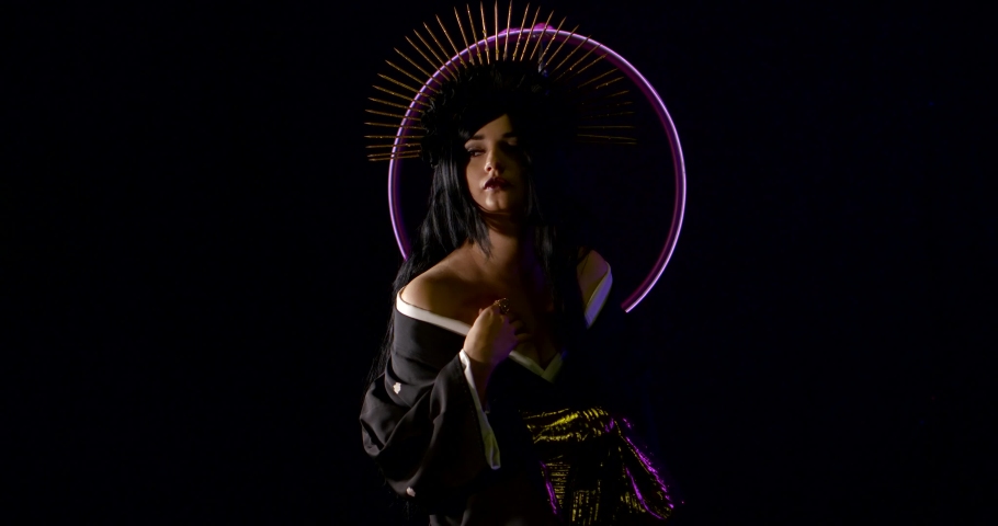 woman dressed in kimono and golden spikes halo crown is standing in dark studio