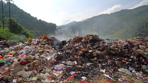Stack of different types of large garbage dump, plastic bags, and trash burning near paddy rice terraces, agricultural fields of Mu Cang Chai, mountain in Vietnam in environmental pollution concept.