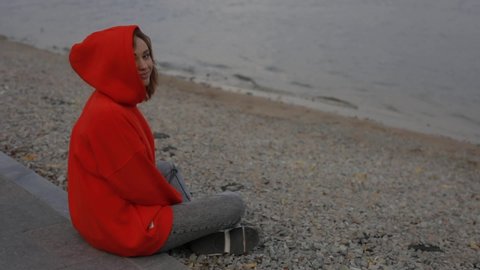 Beautiful woman wear hood sitting at the sea beach in cold autumn day