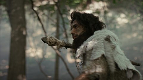 Primeval Caveman Wearing Animal Skin Holds Stone Tipped Spear Looks Around, Explores Prehistoric Forest in a Hunt for Animal Prey. Neanderthal Going Hunting in the Jungle Stockvideó