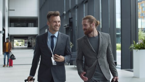 Medium shot of two Caucasian men wearing smart suits going together along airport and having communication