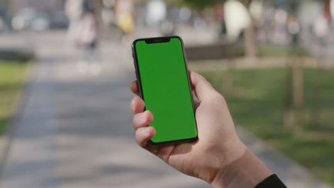 NEW YORK - April 15, 2019: Male hand holding vertical smartphone another hand typing on template greenscreen mock-up showing ok sign at camera. Close-up. Technology and people.