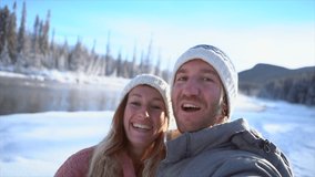 Young couple taking selfie on frozen mountain lake having fun in winter vacations. Couple having video chat outdoors in winter snowy landscape 