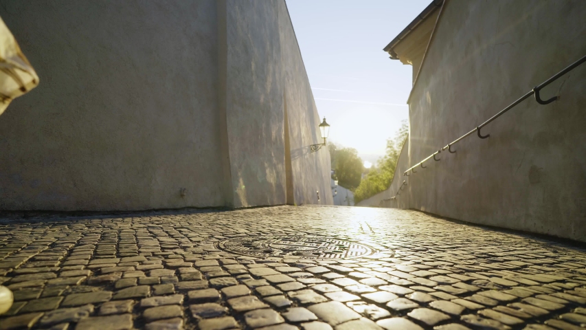 Young woman walking at downtown of Prague. Bottom angle view lady going down the stairway leading to Prague castle. Steady shot, following from the girl whirling and dancing in backlit on empty street