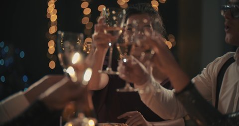 Multiracial young mans and womans wearing fashion wear clinking glasses with champagne, happy asian american and caucasian friends celebrating xmas, new year or birthday party indoors