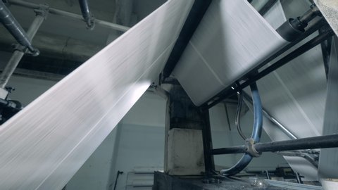 Paper roll is moving through the printing machine. Newspaper printing at a plant.