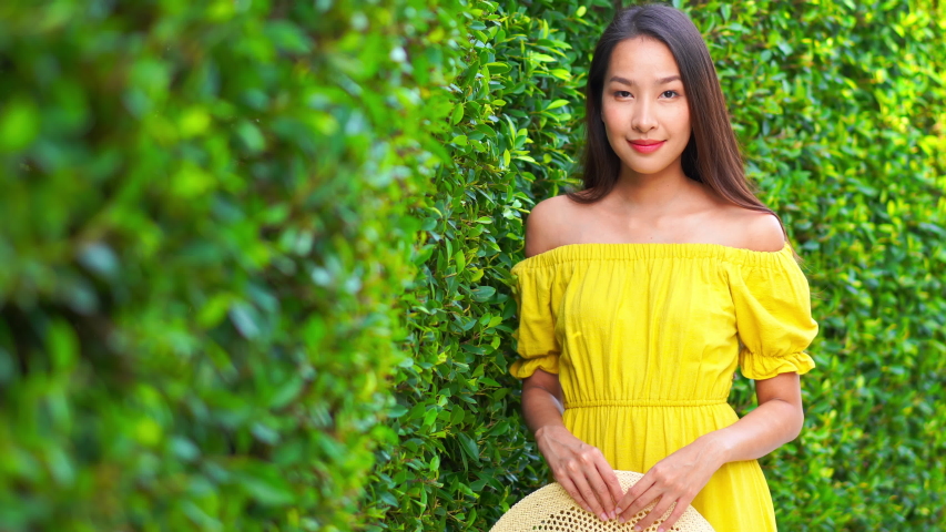 Handheld shot of a young woman smiling at the camera next to a hedge.