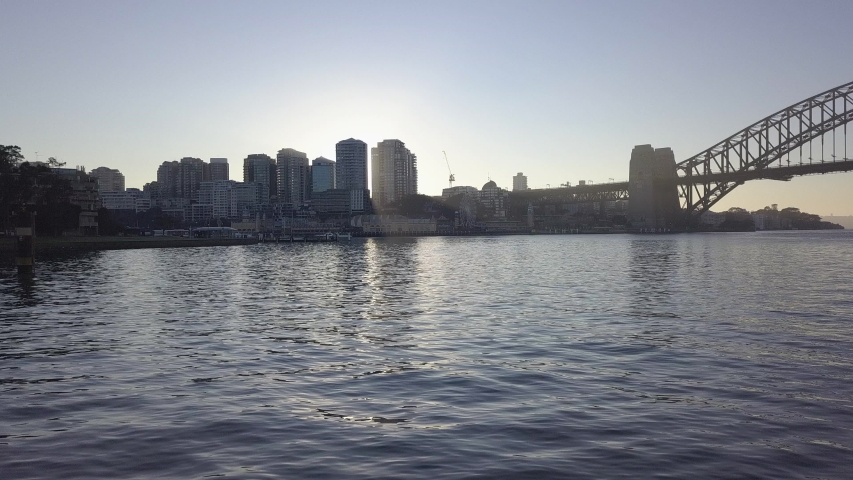 Sun appearing through Sydney CBD skyscrapers from across harbour at sunset
